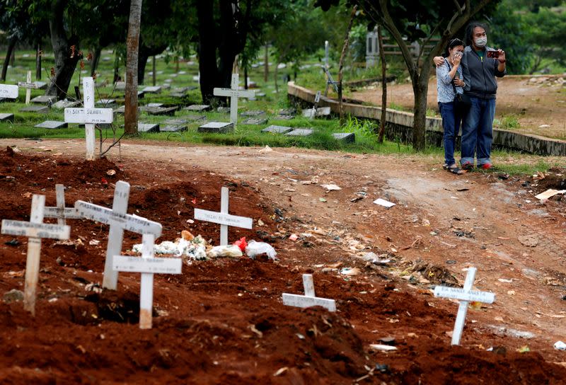 FILE PHOTO: File picture of relatives wearing face masks and standing next to graves of coronavirus disease (COVID-19) victims