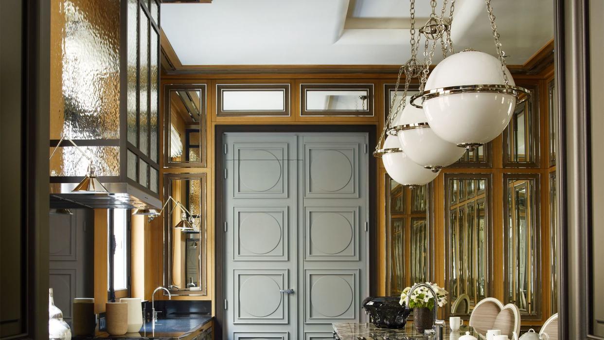 galley kitchen with marble floors in a open weave pattern and dark cabinetry and brown granite countertops wth orb pendant lights over the counter and some frosted glass cabinetry on one side