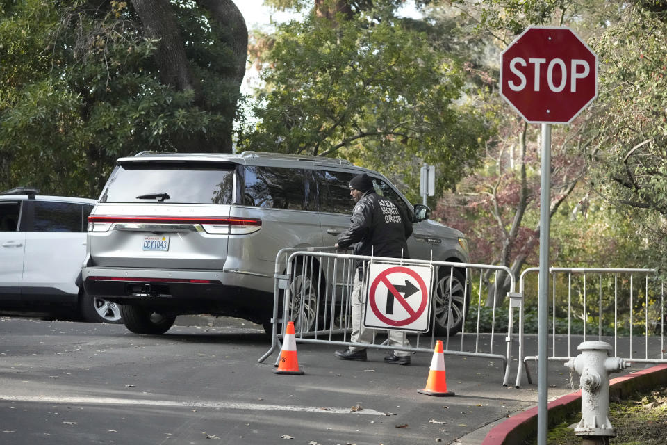 A vehicle allowed to pass drives past a guard closing barricades to a street near the family home of FTX founder Sam Bankman-Fried in Palo Alto, Calif., Friday, Dec. 23, 2022. Bankman-Fried's parents agreed to sign a $250 million bond and keep him at their California home while he awaits trial on charges that he swindled investors and looted customer deposits on his FTX trading platform. (AP Photo/Jeff Chiu)