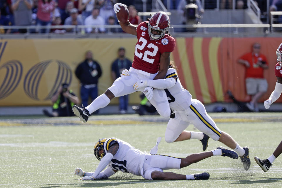 Alabama running back Najee Harris (22) gains yardage as he tries to get past Michigan defensive back Vincent Gray (31) and defensive back DeMarcco Hellams, right, during the first half of the Citrus Bowl NCAA college football game, Wednesday, Jan. 1, 2020, in Orlando, Fla. (AP Photo/John Raoux)