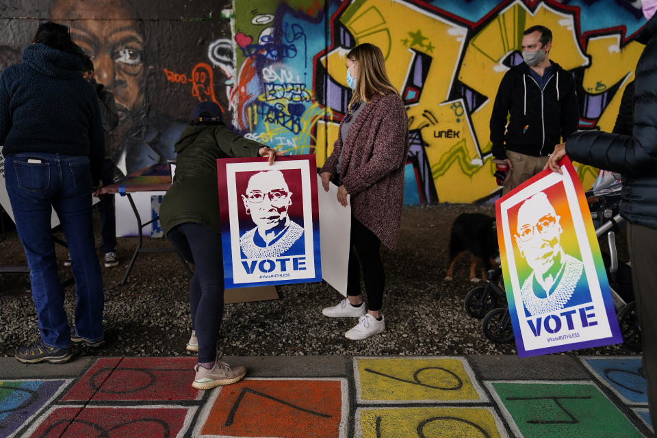 People wait in line holding Supreme Court Justice Ruth Bader Ginsburg posters and wait for artist Brandon Litman to paint a campaign poster after Georgia's Senate runoff race on Sunday, Jan. 10, 2021, in Atlanta. (AP Photo/Brynn Anderson)