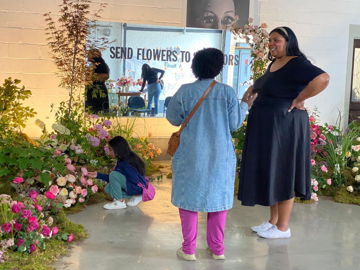 Artist Lauren Palmer, right, discusses the Send Flowers to Survivors floral installation that she and her sisters did with a guest as a young girl crouches to examine the flowers.