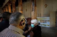 A tourist is helped to wear a mask as a preventive measure against the coronavirus as she visits the Church of the Nativity in Bethlehem in the Israeli-occupied West Bank