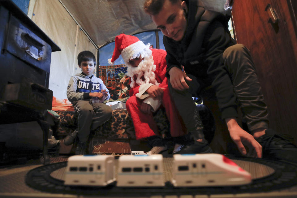 In this photo taken on Sunday, Dec. 15, 2019, Andrei, 19 years old, who lives transit home ran by Florin Catanescu, looks at a toy train brought as a present for the children of a poor family on the outskirts of Brasov, Romania. Thirty years after the 1989 death of Romania's communist-era dictator, the country is still grappling with the ugly legacy of its once-horrific orphanages. Now some of those who grew up abused and unloved in those failed institutions are turning their trauma into commitment. Florin Catanescu, who lived in an orphanage until 1997, now runs a transition home helping those leaving state care to have a better chance of leading meaningful lives.(AP Photo/Vadim Ghirda)