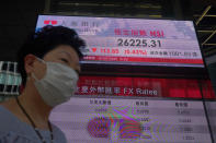 A woman wearing a face mask walks past a bank's electronic board showing the Hong Kong share index at Hong Kong Stock Exchange Tuesday, July 7, 2020. Asian shares were mixed Tuesday, as some benchmarks were buoyed by an ongoing worldwide rally as investors bet on a dramatic economic turnaround amid ongoing challenges of the coronavirus outbreak. (AP Photo/Vincent Yu)