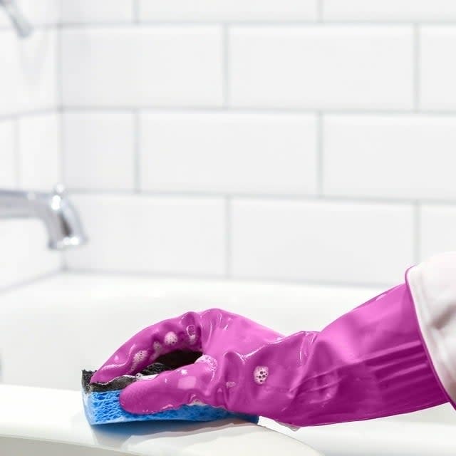 a person scrubbing a bathtub while wearing the gloves