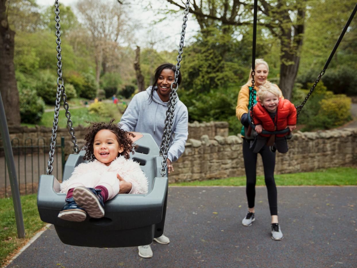 Two moms pushing their children in swings