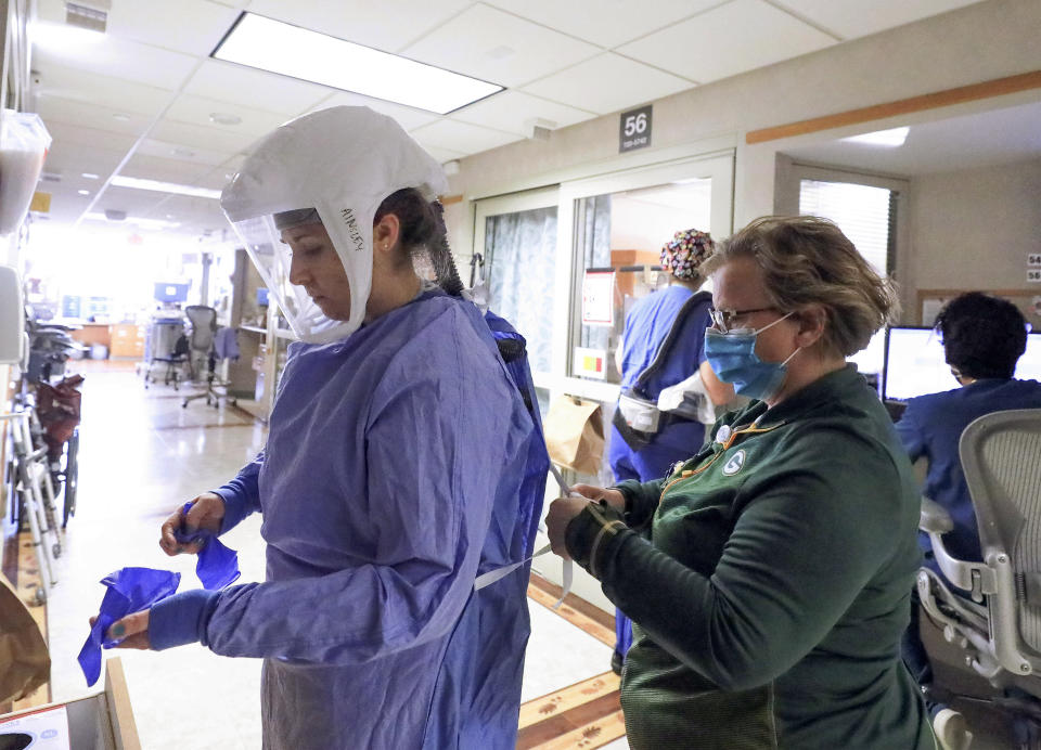 FILE - In this Nov. 5, 2020, file photo, Deb Dalsing, nurse manager of the COVID-19 treatment unit at UW Health assists nurse Ainsley Billesbach with her personal protective equipment at the hospital in Madison, Wis. U.S. hospitals slammed with COVID-19 patients are trying to lure nurses and doctors out of retirement and recruiting nursing students and new graduates who have yet to earn their licenses. (John Hart/Wisconsin State Journal via AP, File)