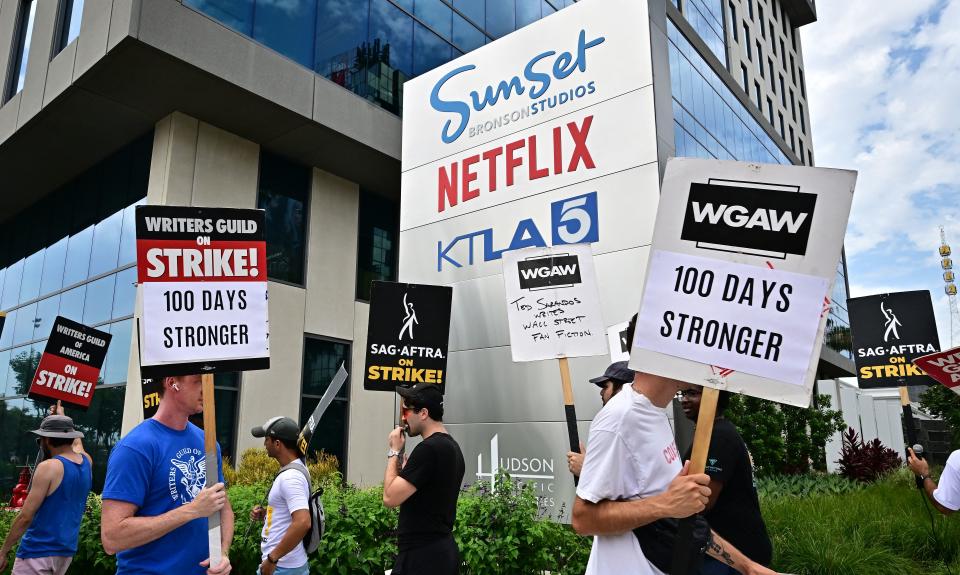 Members hold pickets saying for example: SAG-AFTRA on Strike! and Writers Guild 100 Days Stronger.