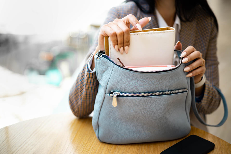 Person at a table putting a wallet into a handbag