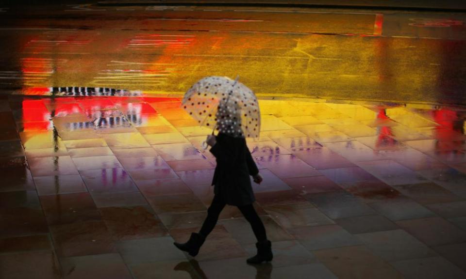 A woman walks on a rain-sodden pavement.