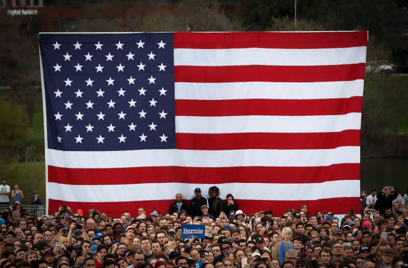 People stand in front of the American flag as Democratic U.S. presidential candidate Senator Bernie Sanders speaks an outdoor campaign rally in Austin