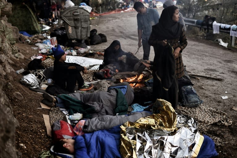 Refugees and migrants warm themselves around a fire after spending a night in a field on the Greek island of Lesbos after crossing the Aegean sea from Turkey on October 5, 2015