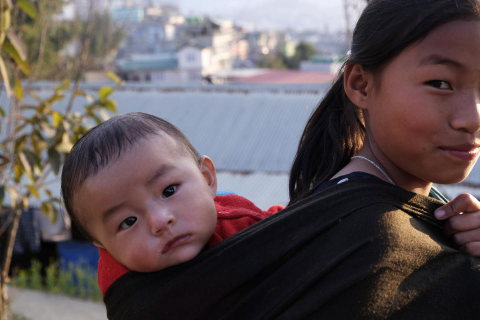 A young Naga girl carrying a child on her back reacts to camera in Kohima, capital of the northeastern Indian state of Nagaland, Sunday, March 1, 2020. Nagaland is home to the indigenous Nagas and borders Myanmar in the east. (AP Photo/Yirmiyan Arthur)