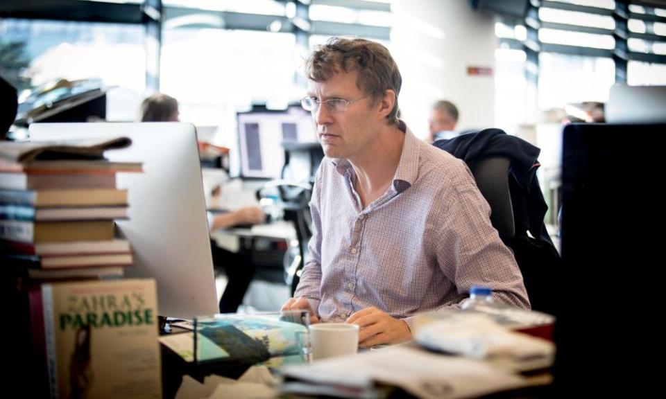 Luke Harding sitting at his desk, looking at a computer, with a pile of books in the foreground