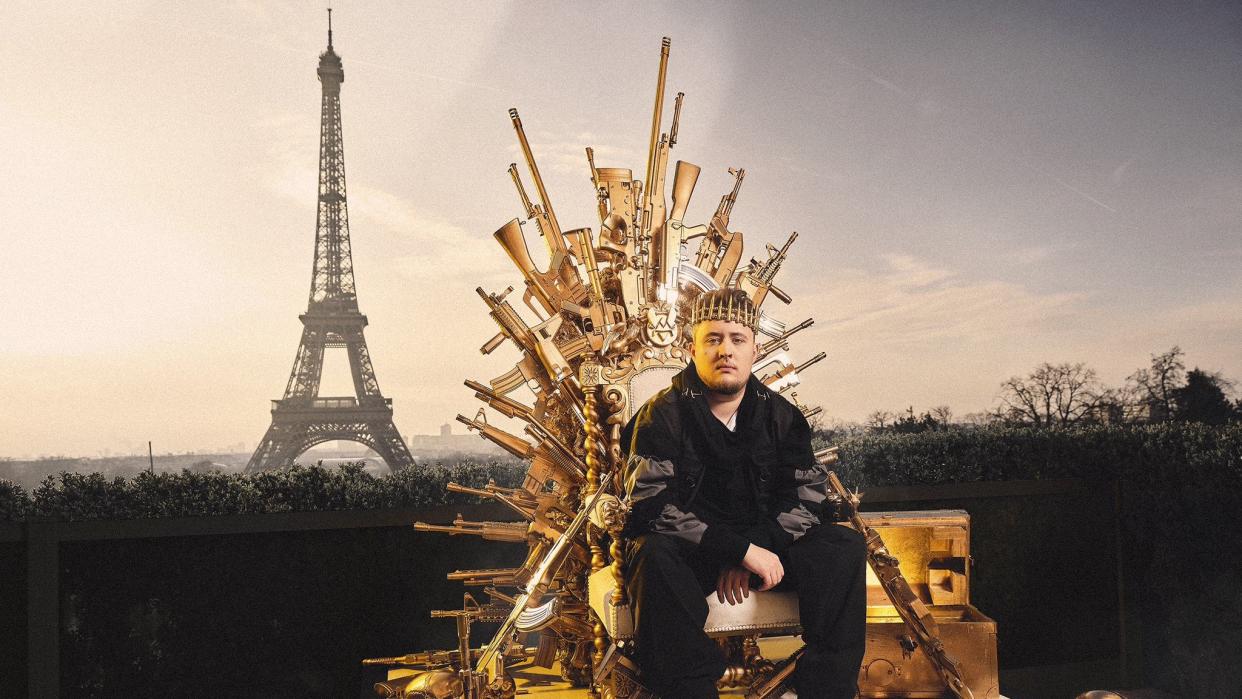  The player Zywoo sits on a golden gun-throne in front of the Eiffel Tower. 