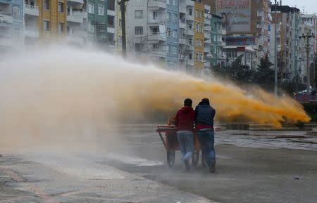 Street vendors take cover as Turkish riot police use a water cannon to disperse Kurdish demonstrators during a protest against the curfew in Sur district, in the southeastern city of Diyarbakir, Turkey, February 21, 2016. REUTERS/Sertac Kayar