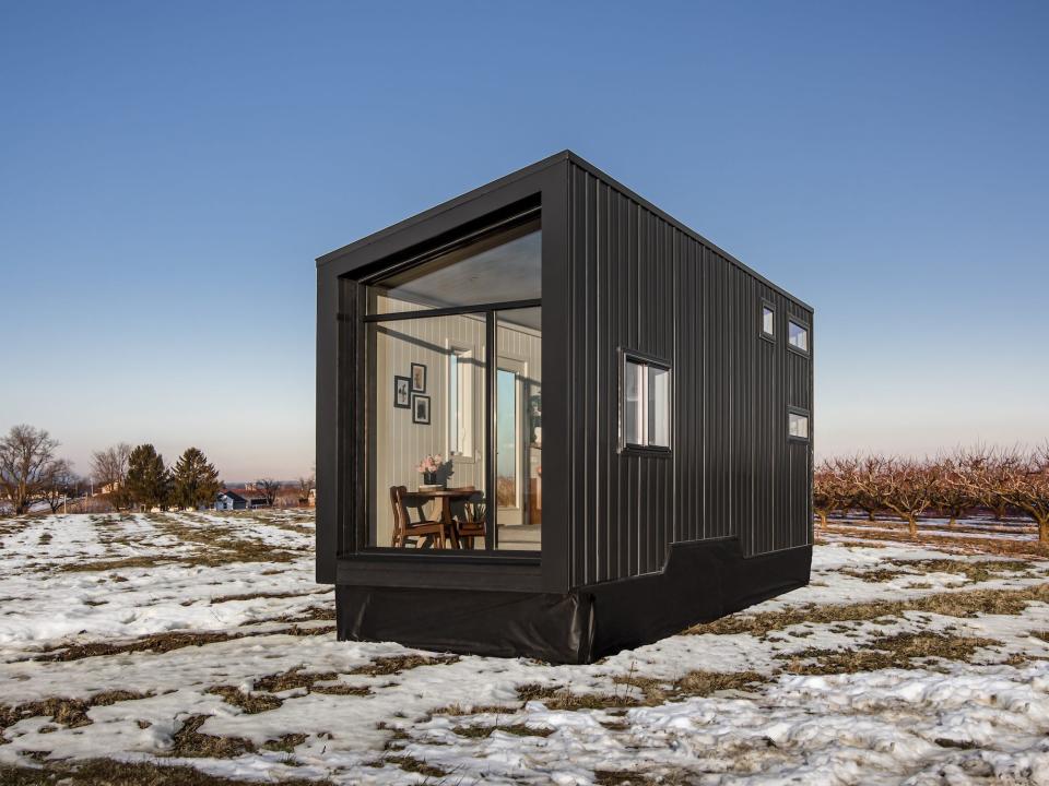 a black tiny home with a large glass wall on a snowy field