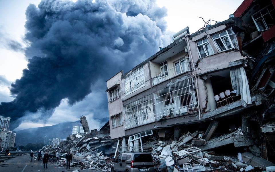 Smoke billows from Iskenderun Port fire as people walk past collapsed building - Getty