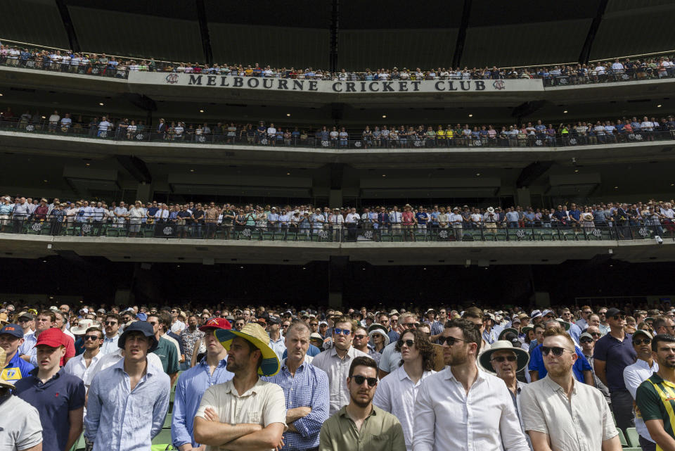 Spectators stand during a tribute to late Australian cricketers Shane Warne and Andrew Symonds ahead of play of the second cricket test between South Africa and Australia at the Melbourne Cricket Ground, Australia, Monday, Dec. 26, 2022. (AP Photo/Asanka Brendon Ratnayake)