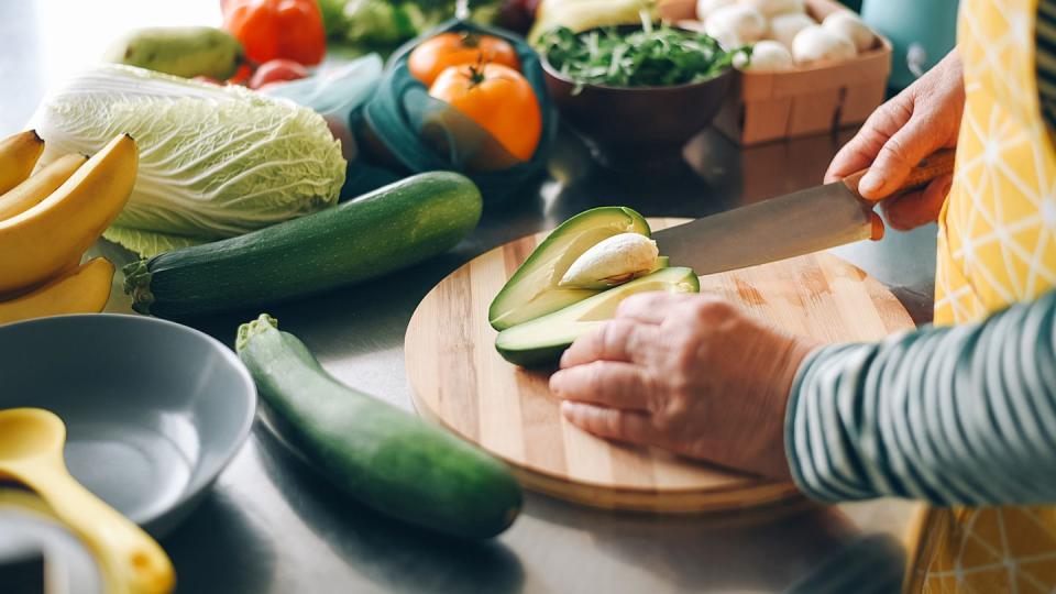a woman cuts a ripe avocado and takes out a stone from it on a wooden plank fresh vegetables salad preparation diet food ecological products