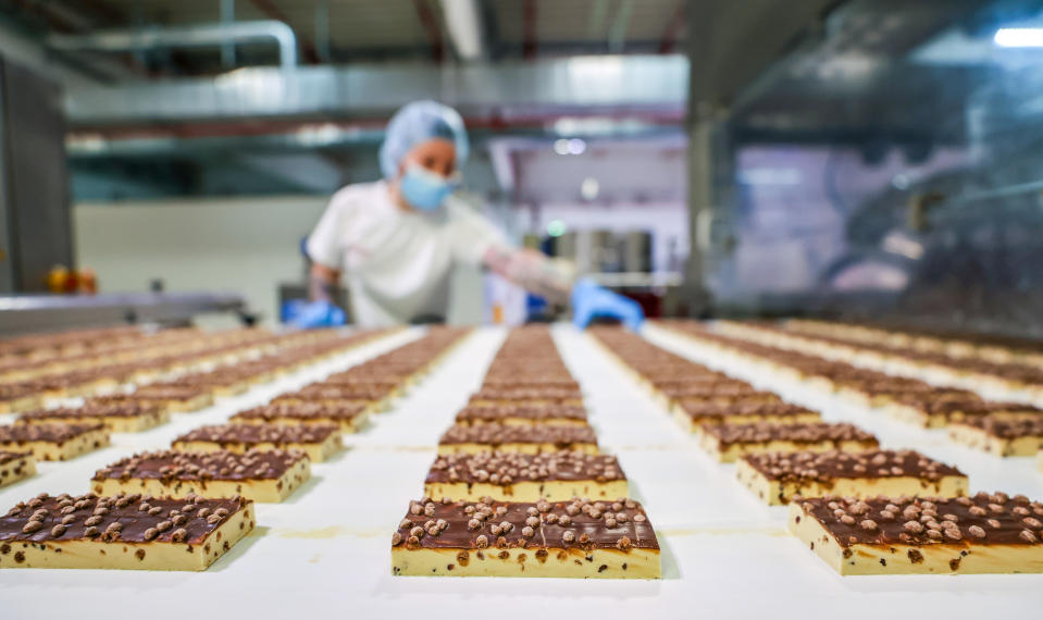Worker in protective gear oversees chocolate chip bar production line