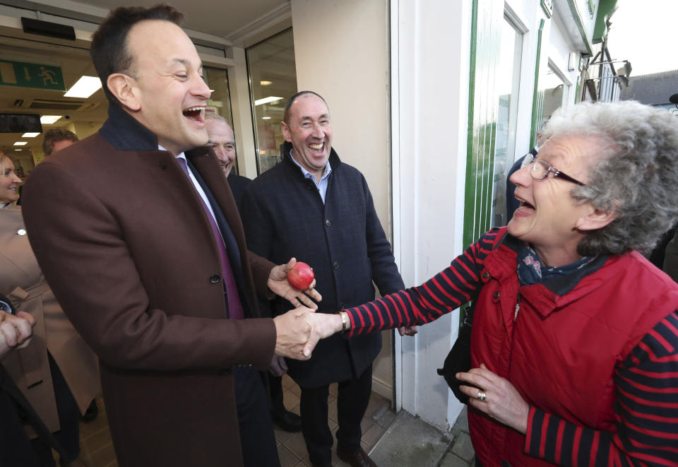 Ireland's Prime Minister Leo Varadkar, left, and Fine Gael candidate Pat Deering, share a joke with Patricia Cremin Hegerty after she handed the Taoiseach an apple while he was canvassing in Tullow, Co Carlow, Ireland, Thursday Feb. 6, 2020. Ireland goes to the polls for a general election on Feb. 8. (Niall Carson/PA via AP)