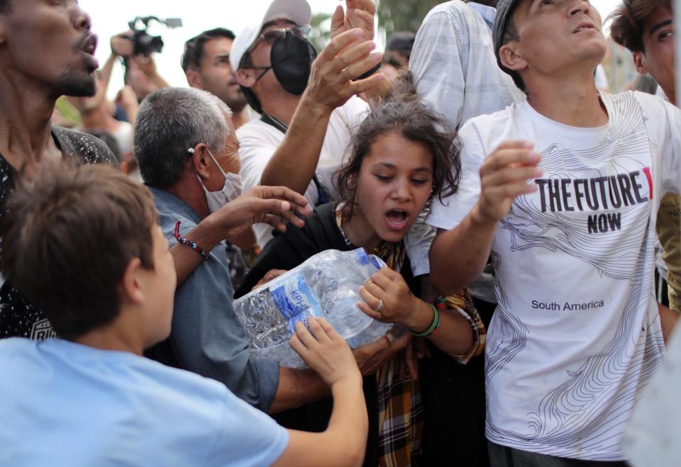 Migrants scuffle to take bottles of water during a distribution by local authorities near Mytilene town, on the northeastern island of Lesbos, Greece, Saturday, Sept. 12, 2020. Thousands of asylum-seekers spent a fourth night sleeping in the open on the Greek island of Lesbos, after successive fires destroyed the notoriously overcrowded Moria camp during a coronavirus lockdown. (AP Photo/Petros Giannakouris)