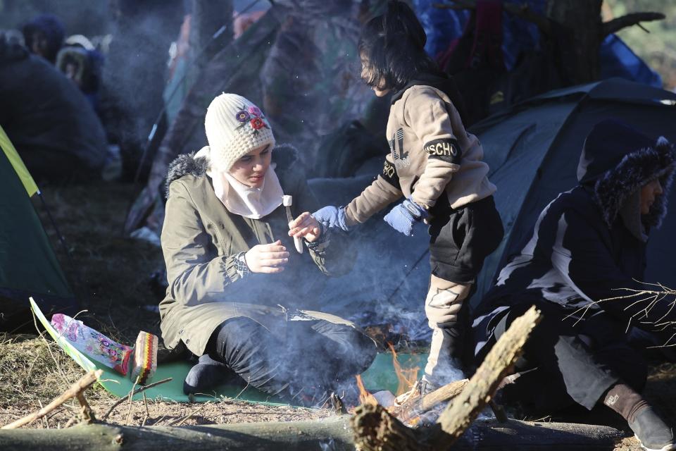 A woman and her child eat as they gather with other migrants from the Middle East and elsewhere at the Belarus-Poland border near Grodno, Belarus, Tuesday, Nov. 9, 2021. Polish riot police faced off Tuesday against migrants, including families with young children, who were camped just across the border in Belarus, amid a tense standoff on the European Union's eastern border. (Leonid Shcheglov/BelTA via AP)