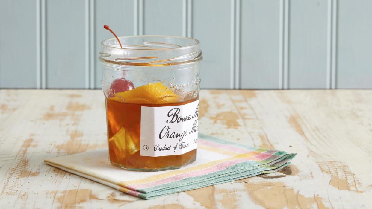 a marmalade jar with a drink in it, with a cherry and orange peel garnish