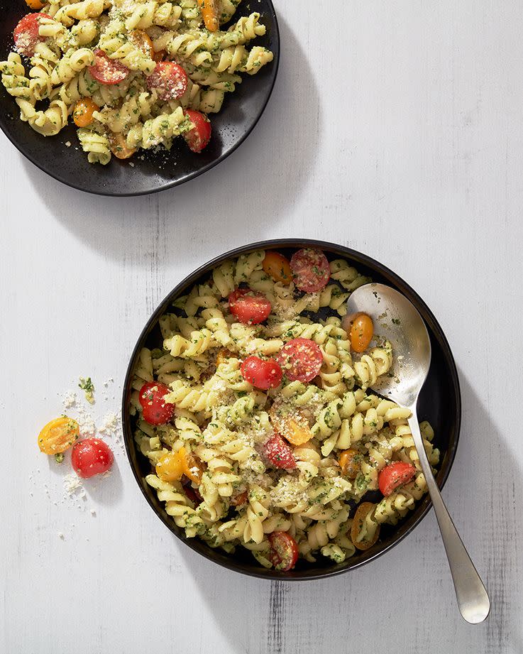 pesto pasta salad with halved grape tomatoes topped with parmesan in a black bowl