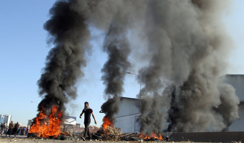 A demonstrator walks near burning tires during ongoing anti-government protests in Tripoli