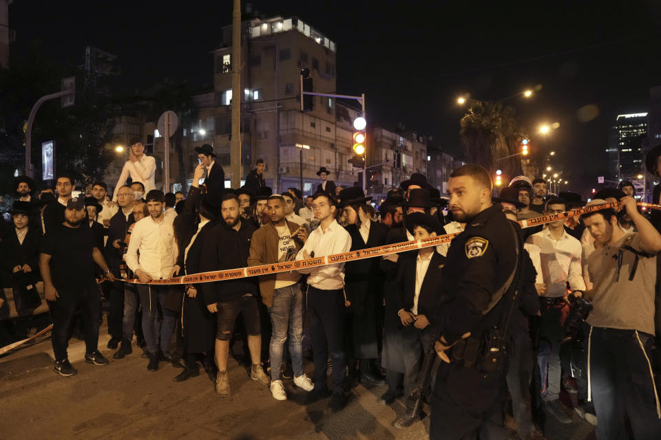 A crowd gathers to watch police working at the site where a a gunman opened fire in Bnei Brak, Israel, Tuesday, March 29, 2022. The circumstance of the deadly incident in the city east of Tel Aviv were not immediately clear. (AP Photo/Oded Balilty)