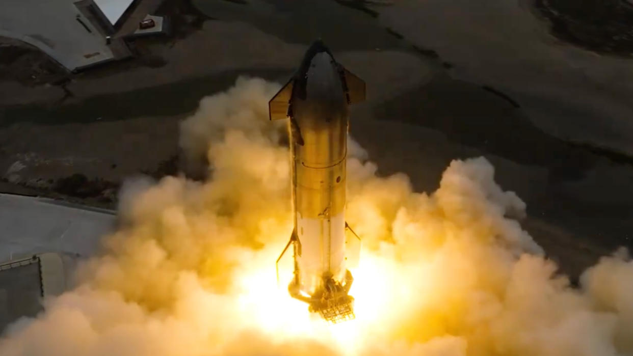  Fire, dust and exhaust billow from the base of a big, stainless steel rocket. 