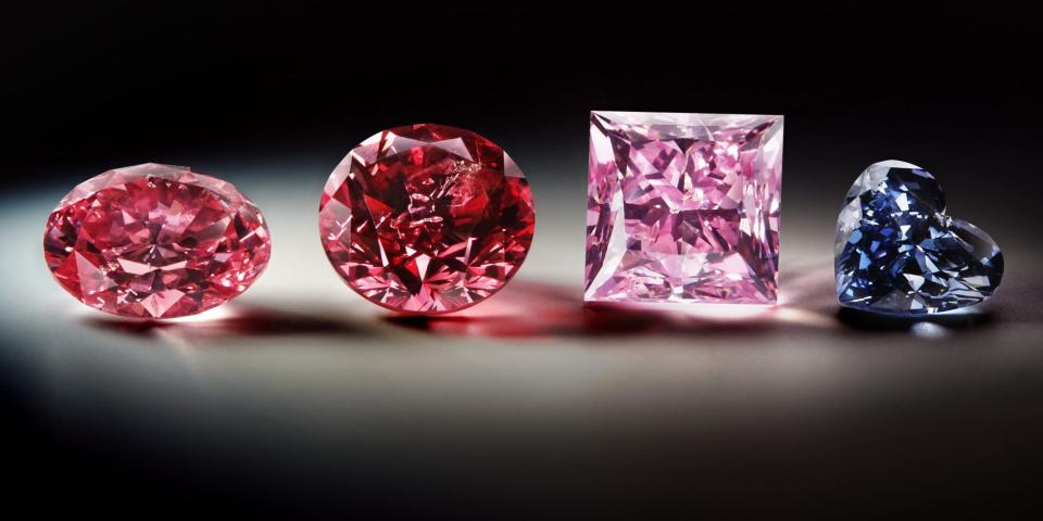 A photo of four diamonds, from magenta to clear blue, on a spotlight background.