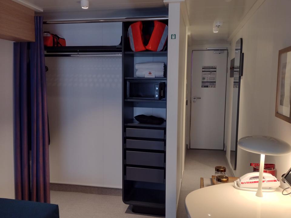 A cruise cabin with an open closet and desk facing the door.