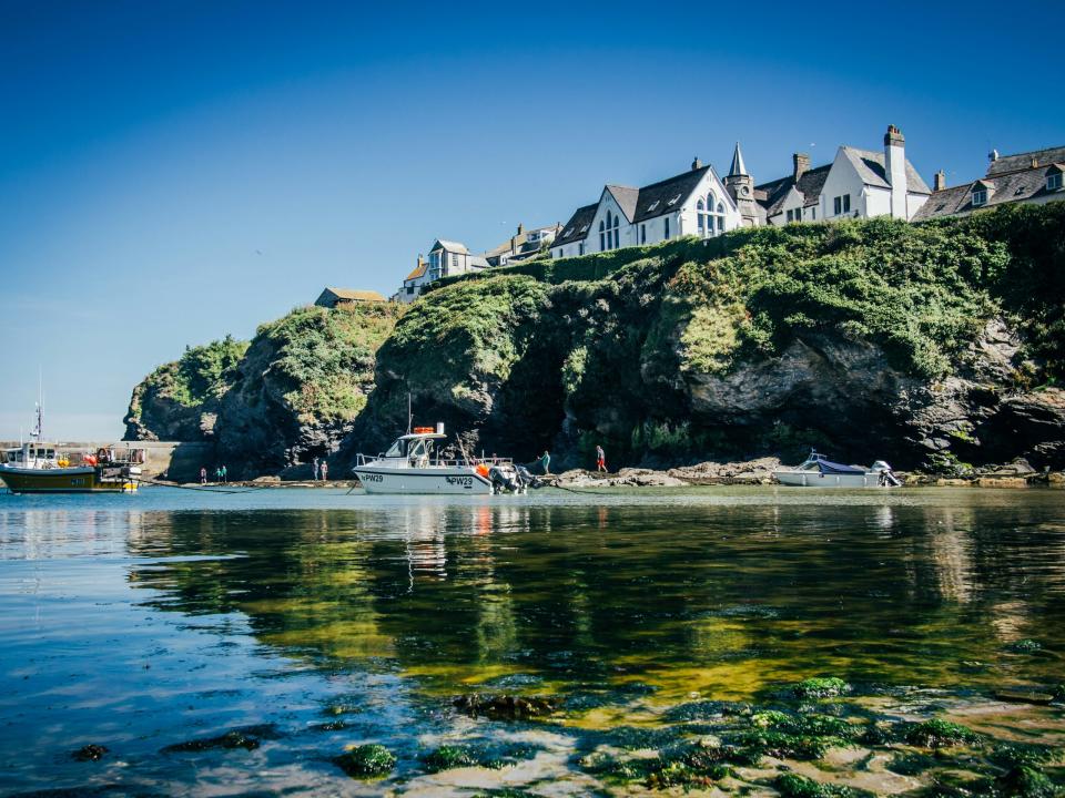 Port Isaac is the village where the series “Doc Martin” is filmed. 
Pictured: the coast of Port Isaac with boats and houses seen on the edge of the cliffs