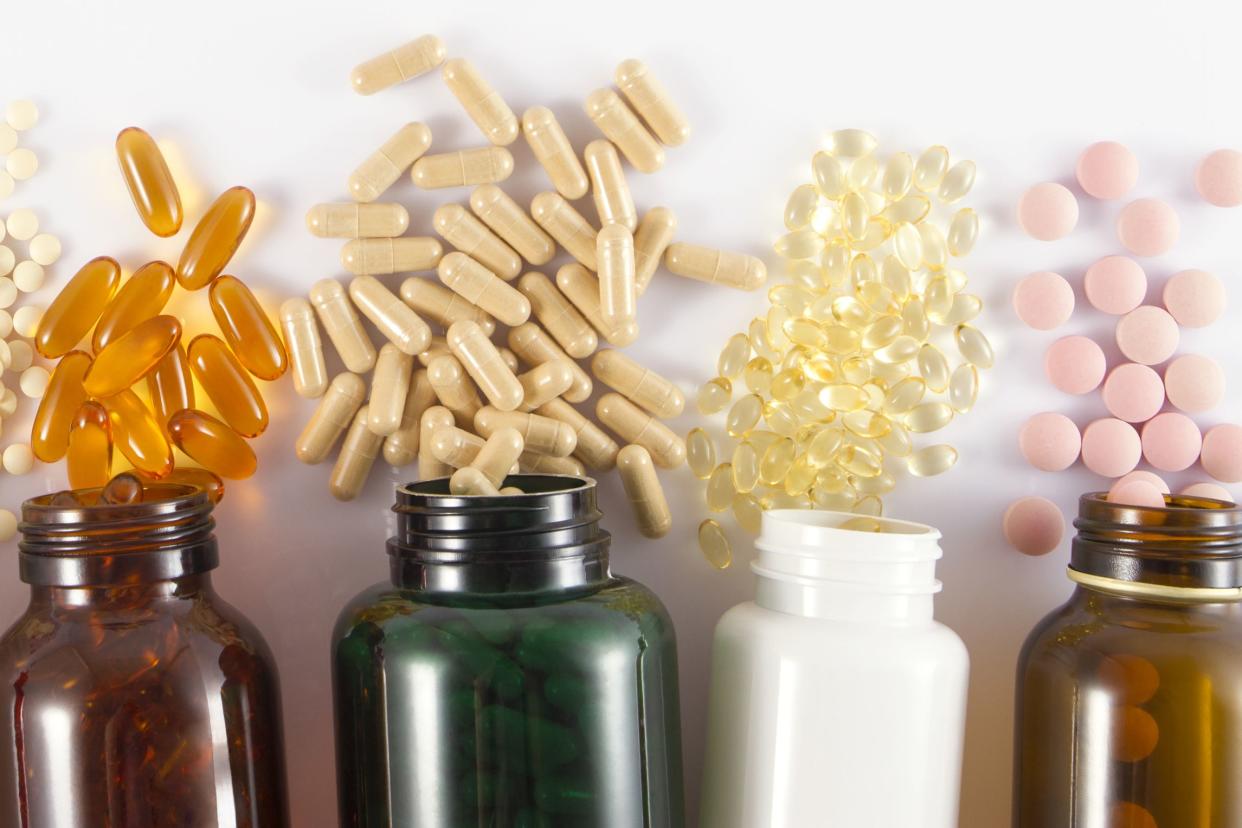 Top-view of four vitamin bottles, in a line, spilled different vitamins on a white background