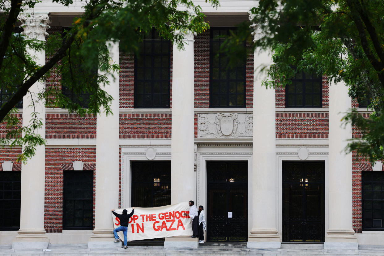 People putting up a sign outside a building: Stop the Genocide in Gaza.