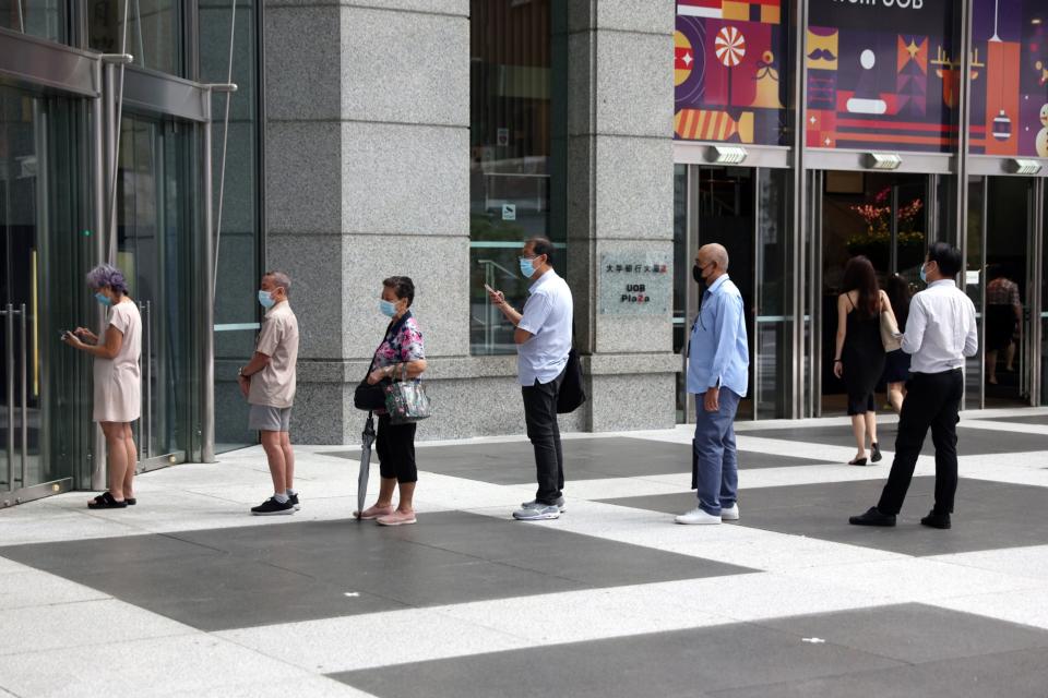 People in masks stand in line outside a bank in Singapore in January.