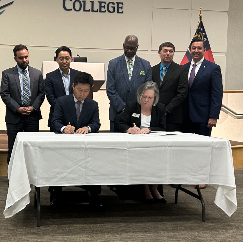 Officials from Hyundai and Savannah Technical College look on as Oscar Kwon, CEO and president of Hyundai Motor Group Metaplant America and Kathy Love, president of STC sign the agreement for the Electric Vehicle Professional certificate.