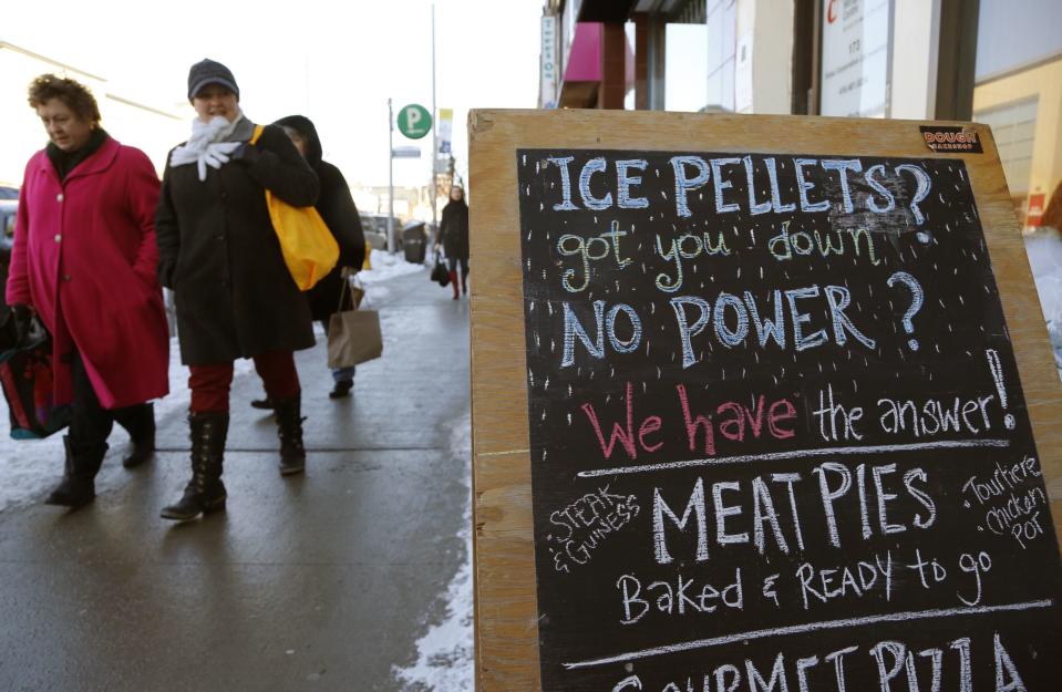 Christmas shoppers walk past a bakery advertising hot meat pies for residents whose electricity remains knocked out by an ice storm in Toronto