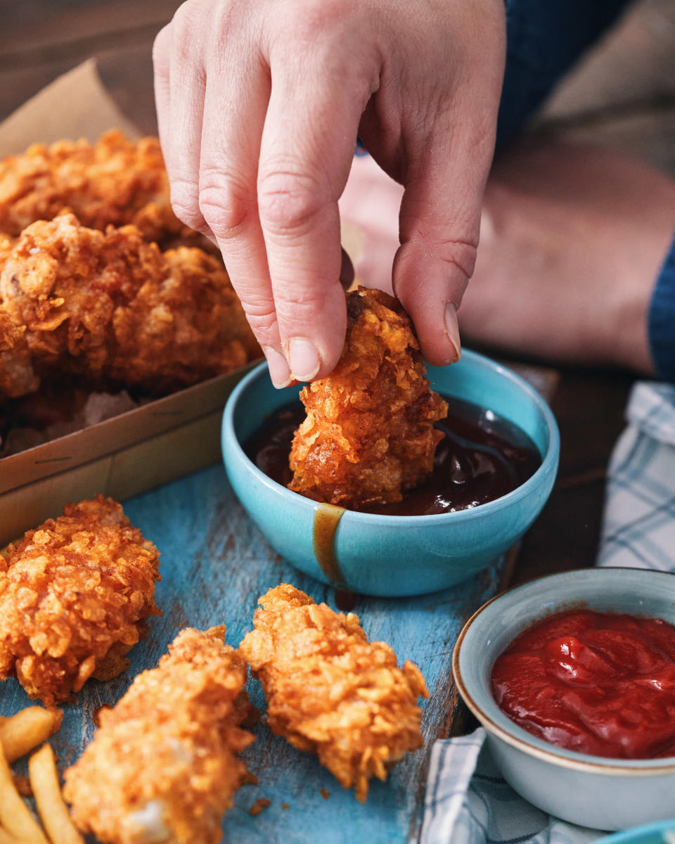 An image of a person's hand dipped a piece of fried chicken into a small blue bowl of barbeque sauce.