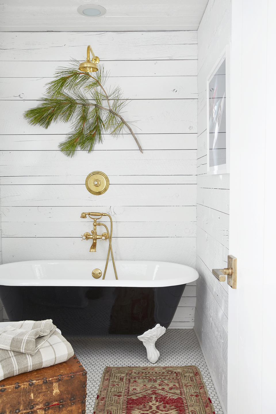 winter christmas cabin bathroom with black clawfoot tub and a red vintage rug acting as a bath mat