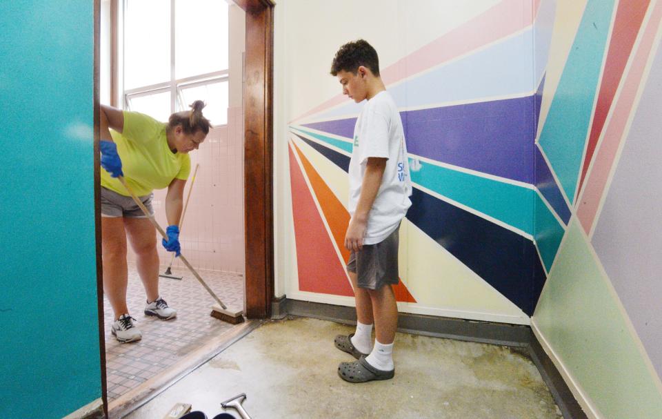 Jamie Travis, left, ServErie site lead at Woodrow Wilson Middle School, cleans a girls bathroom at the school in Erie on Friday. Beckett Caplan, 13, right, earlier helped paint the graphic design on the wall.