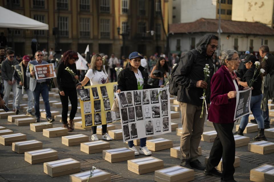 People walk among boxes representing symbolic coffins as they remember former guerrillas and social leaders who have been killed since the 2016 signing of a peace agreement between rebels of the Revolutionary Armed Forces of Colombia, FARC, and the government, in Bogota, Colombia, Tuesday, Feb. 20, 2024. (AP Photo/Fernando Vergara)