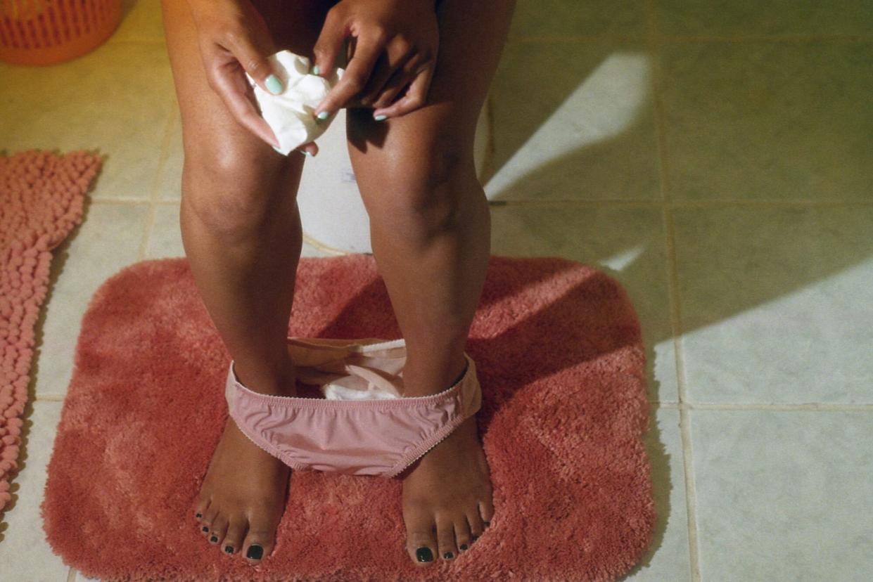 Woman In Bathroom on Toilet with Implantation Bleeding