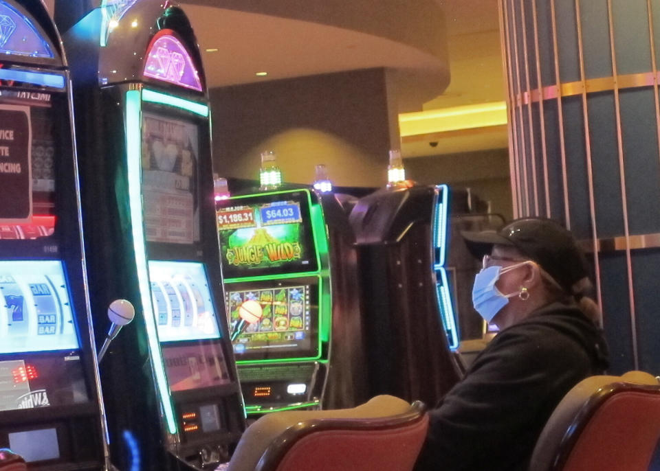This May 3, 2021 photo shows an intentionally disabled slot machine next to a woman playing a different slot machine while wearing a face mask at the Hard Rock casino in Atlantic City, N.J. On Friday, May 28, New Jersey dropped its indoor mask mandate and Atlantic City casinos turned slot machines that were disabled to create distance between players back on again. (AP Photo/Wayne Parry)