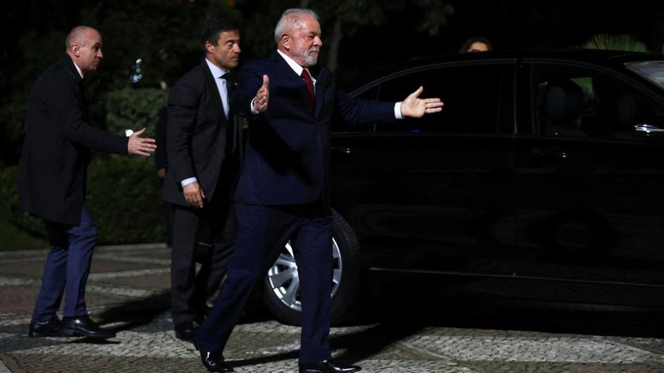 Lula caminha perto de carro e de seguranças e faz gesto de abrir os braços