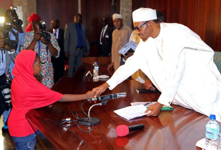 A girl representing the Chibok schoogirls presents a document to President Mohammadu Buhari (R) during a meeting between members of the Bring Back Our Girls group and the president in Abuja, on July 8, 2015 (AFP Photo/Philip Ojisua)